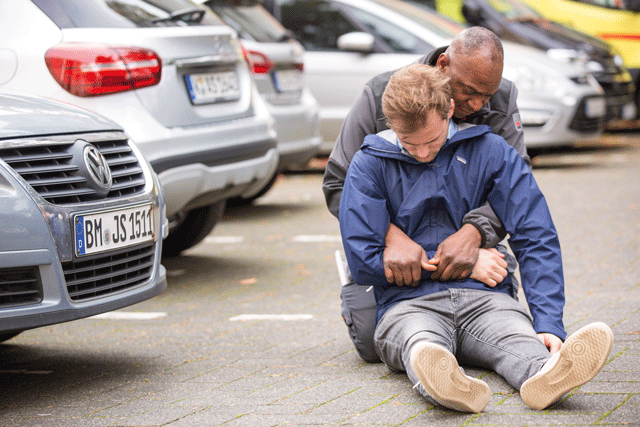Erste Hilfe Angebote Eine bewusstlose Person wird mittels dem Rettungsgriff von der Straße gezogen.