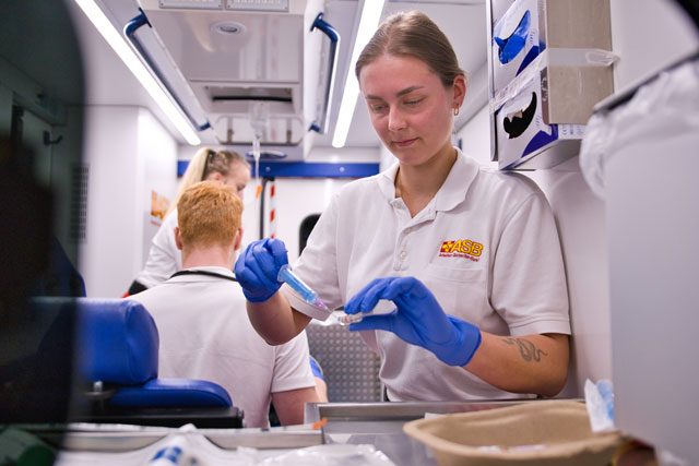 Mitarbeiterin des ASB Reginalverbands Frankfurt die zum aktuellen Zeitpunkt mittels einer Spritze ein Medikament, in einem RTW aufzieht. Die anderen Kollegen und Kolleginnen kümmern sich in der Zeit um den Patienten. 